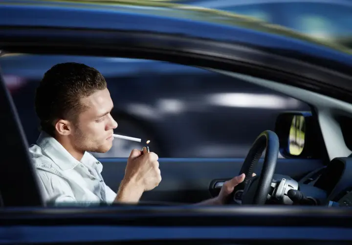 Joven enciende cigarrillo mientras se puede fumar conduciendo.