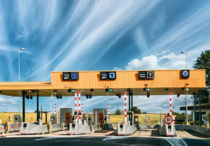 Estación de ap2 peajes bajo un cielo azul con nubes. Carriles de pago con barreras y señales de tráfico.