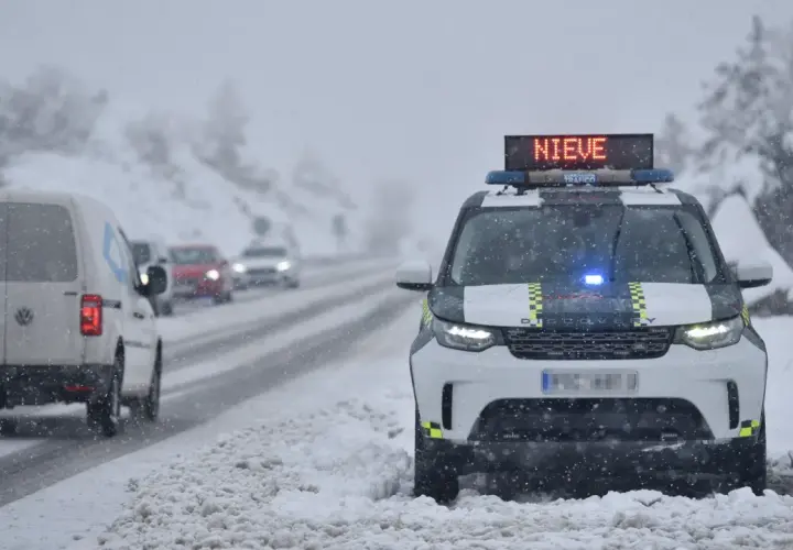 DGT alerta de nieve en carreteras. Un coche patrulla con luces azules y el mensaje "NIEVE" en su panel luminoso se detiene en un arcén nevado.
