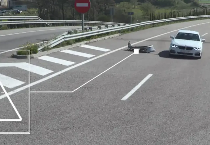 Un coche blanco se detiene cerca de un parachoques dañado en la carretera, indicando un accidente por objeto en la carretera.