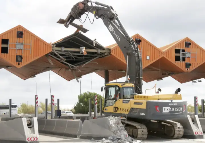 Excavadora derribando el peaje de Cubelles. La estructura naranja se desmorona mientras la máquina trabaja.