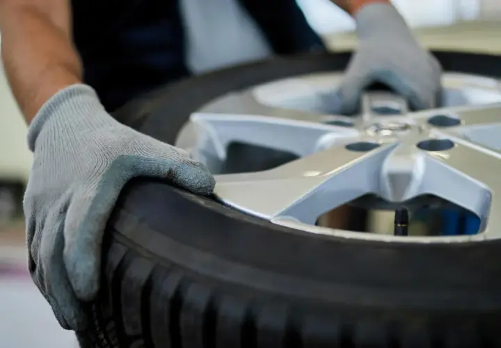 Manos enguantadas sostienen un neumático y llanta, listos para su reparación.