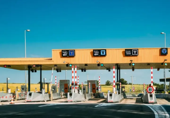 Peaje en la a6 autovía, con barreras rojas y blancas, señales de tráfico y un cielo azul despejado.