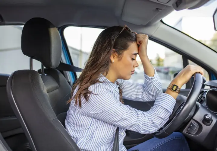 Mujer con la mano en la frente, sufriendo ansiedad al conducir.