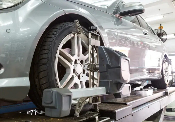 Un coche plateado en un taller mecánico recibe servicio de alineación de ruedas con equipo especializado.
