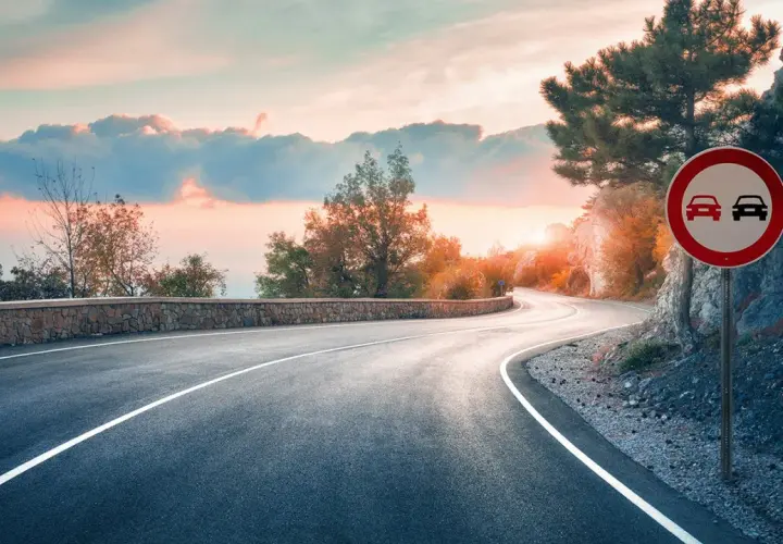 Carretera sinuosa al atardecer. Señal de prohibido adelantar en curvas.