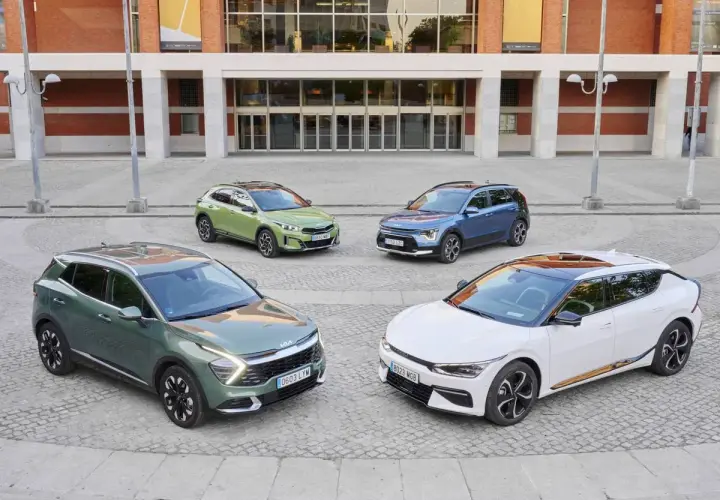 Cuatro coches Kia, dos hibridos y electricos, en tonos verde, azul y blanco, frente a un edificio moderno.