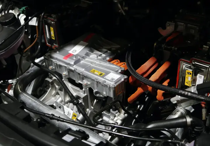 Detalles del motor de un coche eléctrico, listo para su revisión. Cables naranjas de alta tensión y componentes metálicos.
