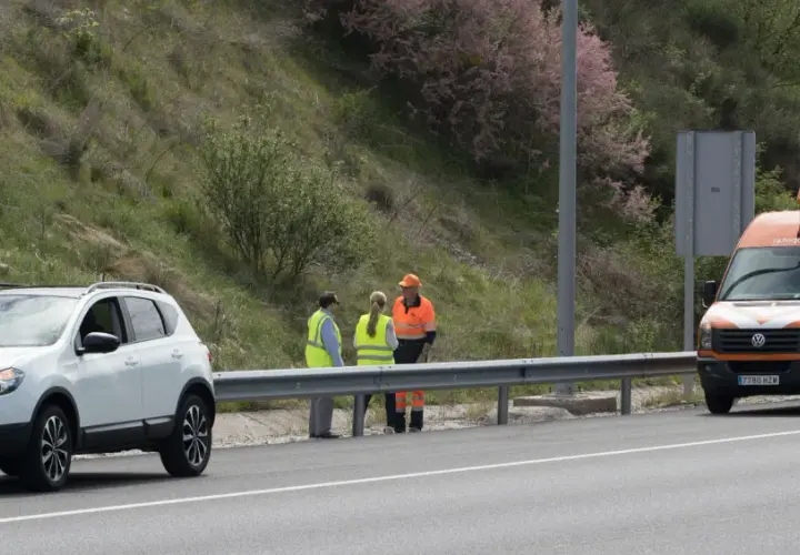 Personal de autopistas atiende un incidente en la carretera. Un coche blanco y una furgoneta naranja con señalización de emergencia están detenidos.