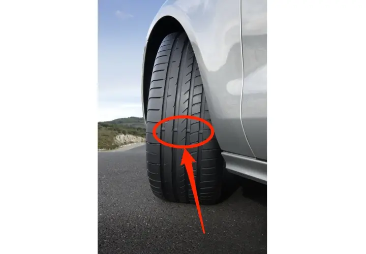 Flecha roja señala los neumáticos desgastados de un coche plateado en una carretera.