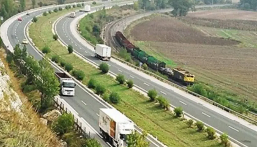Autopista con camiones y tren de carga. Un viaje escénico de Burgos a Zaragoza sin peaje, con paisajes verdes y campos.