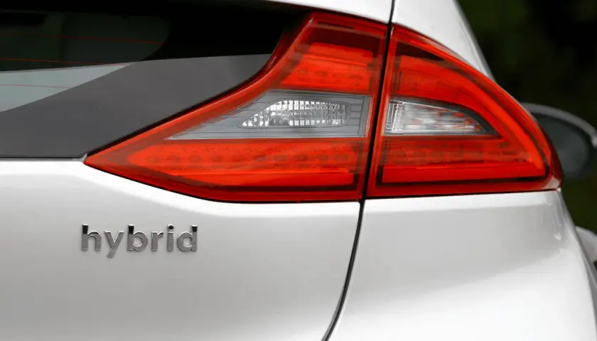 Detalle de la parte trasera de un coche blanco con la palabra "hybrid" en relieve. Las luces traseras rojas y blancas son visibles.