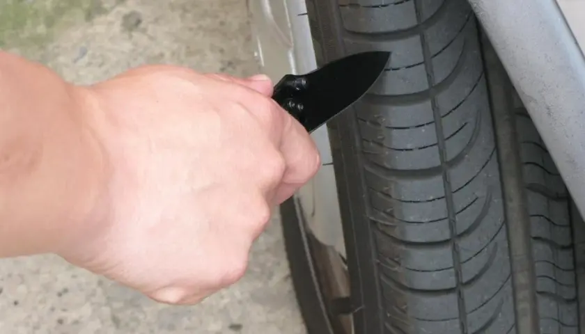 Mano con navaja revisando la banda de rodadura de un neumático, para saber si tengo una rueda pinchada.