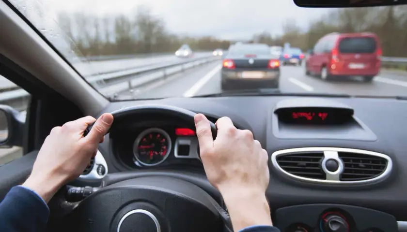 Manos al volante en carretera con tráfico. Mantener una distancia de frenado segura depende de la atención.