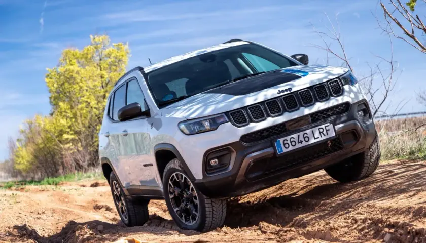 El Jeep Compass Trailhawk 4xe blanco se aventura por un camino de tierra, demostrando su capacidad todoterreno bajo un cielo azul.