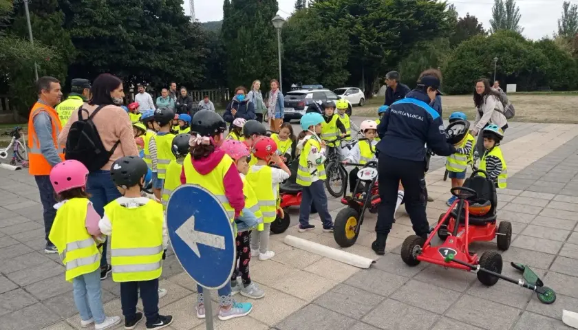 Niños con chalecos reflectantes participan en juegos de educación vial, aprendiendo normas de tráfico con bicicletas y coches de pedales.