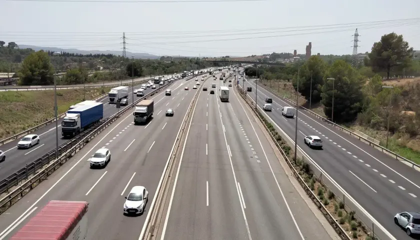 Tráfico intenso en la ap7 Girona, con camiones y coches circulando por la autopista bajo un cielo despejado.