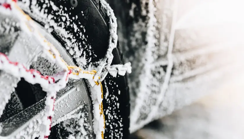 Primer plano de cadenas de nieve cubiertas de escarcha sobre un neumático de coche, mostrando cómo colocar cadenas de nieve para la seguridad invernal.