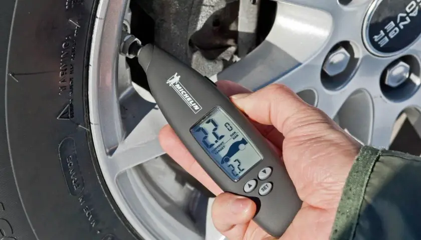 Mano revisa la presión neumaticos con un medidor digital Michelin. Muestra 2.2 bares de presión actual y objetivo.