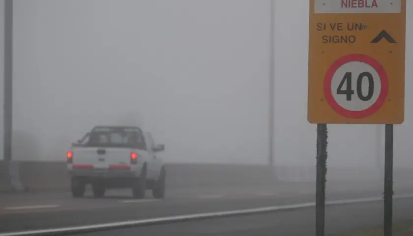 Camioneta blanca avanza en **niebla densa** bajo un **alumbrado** de señalización vial que indica 40 km/h.
