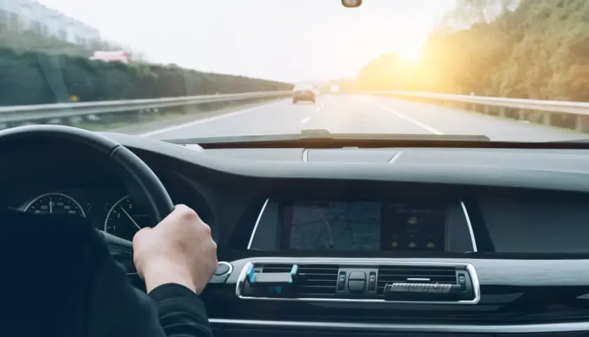 Conduciendo por la autopista, el sol brilla al atardecer. El navegador muestra la ruta, anticipando el pago del vía t peaje.