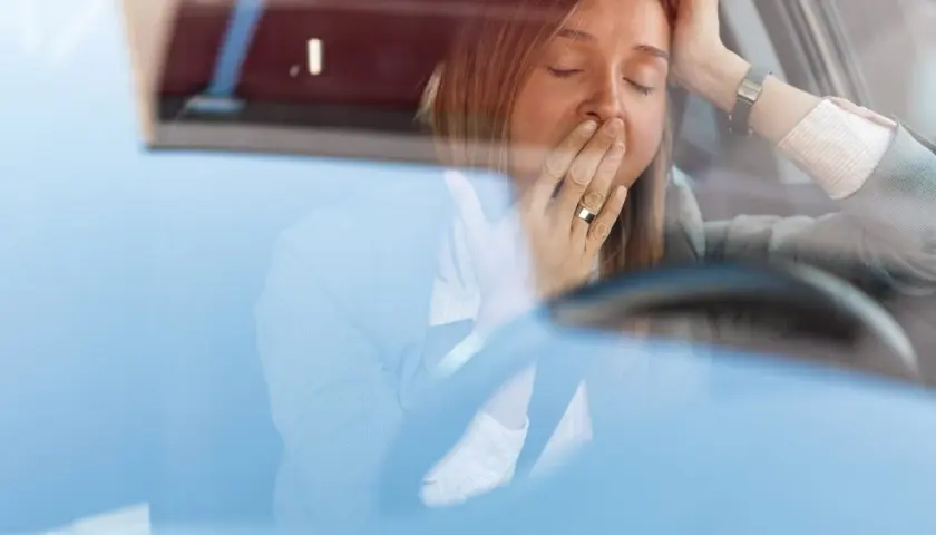 Mujer bostezando en el coche. Para disminuir la probabilidad de somnolencia debe evitar conducir.