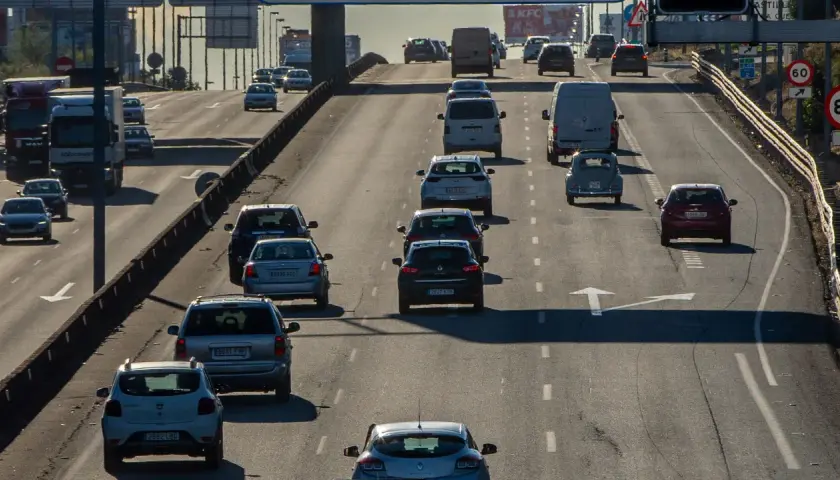 Tráfico denso en autopista, con coches y furgonetas circulando. Se observa señal de tráfico con **mínimo de velocidad en autopista** de 60 km/h.