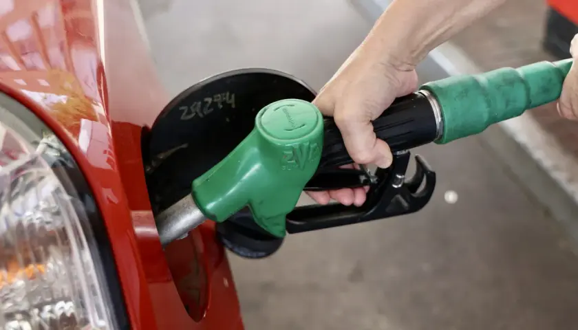 Mano repostando un coche rojo con una manguera de combustible verde. El futuro de los coches diésel aún depende de la gasolina.