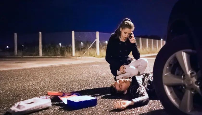 Una mujer llama a emergencias junto a un hombre tendido en la carretera. A su lado, un botiquín abierto. ¿Qué significa pas? ¿Una vida en peligro?