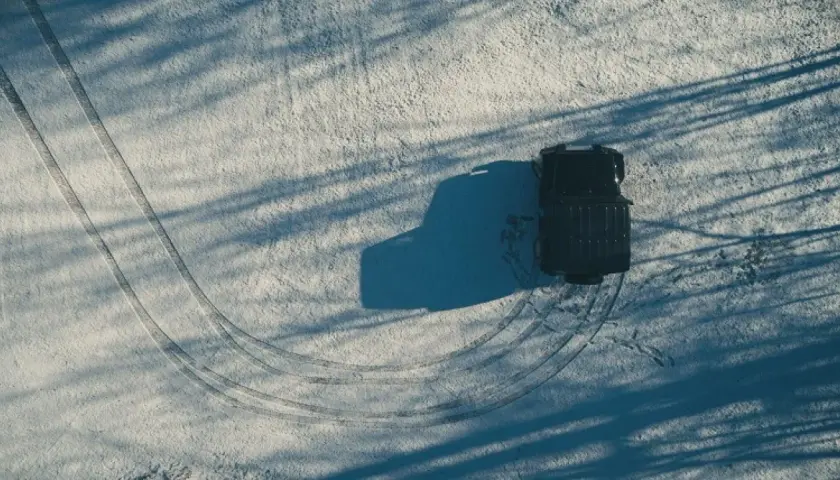 Un vehículo negro deja huellas en la nieve, mostrando cómo conducir con hielo.