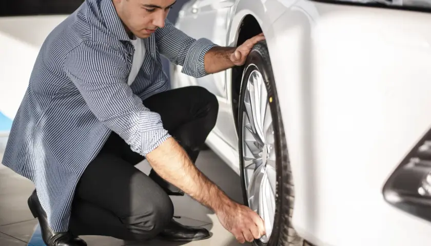 Hombre revisando la rueda de un coche blanco, asegurándose de que el neumático tenga el código velocidad correcto para un viaje seguro.