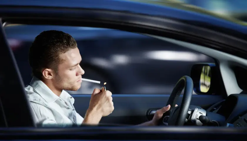 Joven enciende cigarrillo mientras se puede fumar conduciendo.