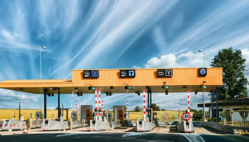 Estación de ap2 peajes bajo un cielo azul con nubes. Carriles de pago con barreras y señales de tráfico.