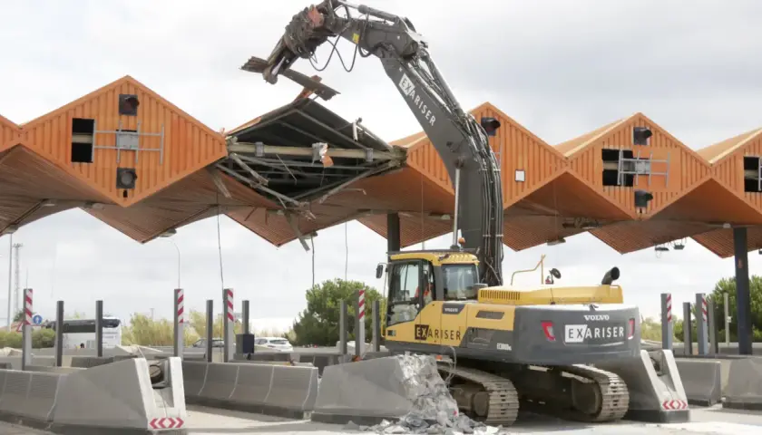 Excavadora derribando el peaje de Cubelles. La estructura naranja se desmorona mientras la máquina trabaja.