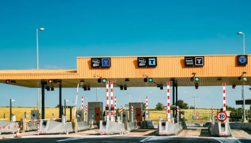 Peaje en la a6 autovía, con barreras rojas y blancas, señales de tráfico y un cielo azul despejado.