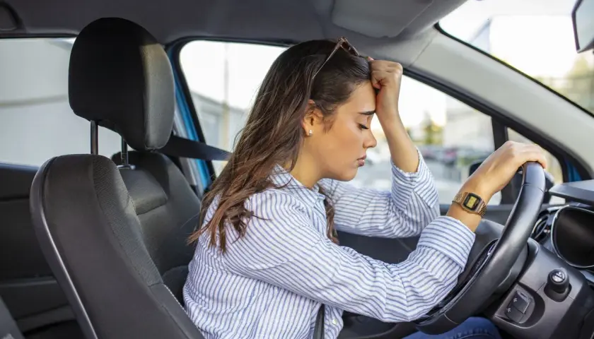 Mujer con la mano en la frente, sufriendo ansiedad al conducir.