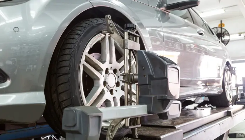 Un coche plateado en un taller mecánico recibe servicio de alineación de ruedas con equipo especializado.