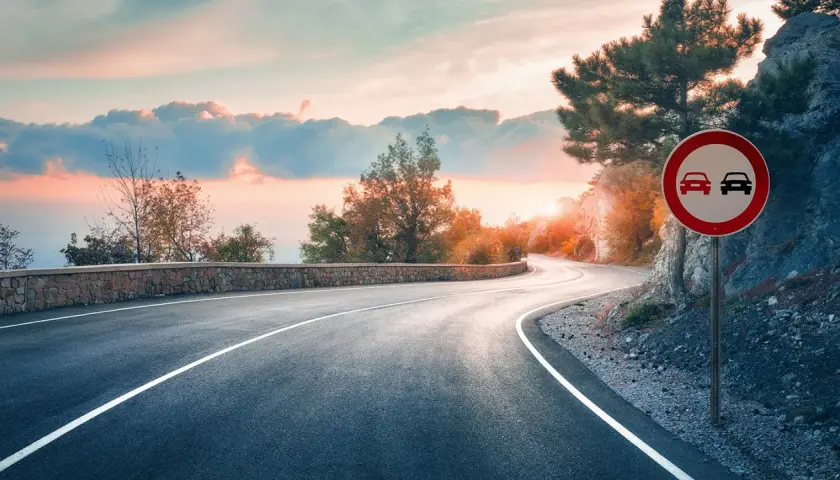 Carretera sinuosa al atardecer. Señal de prohibido adelantar en curvas.