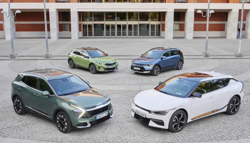 Cuatro coches Kia, dos hibridos y electricos, en tonos verde, azul y blanco, frente a un edificio moderno.