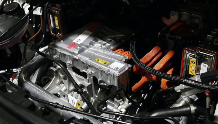 Detalles del motor de un coche eléctrico, listo para su revisión. Cables naranjas de alta tensión y componentes metálicos.