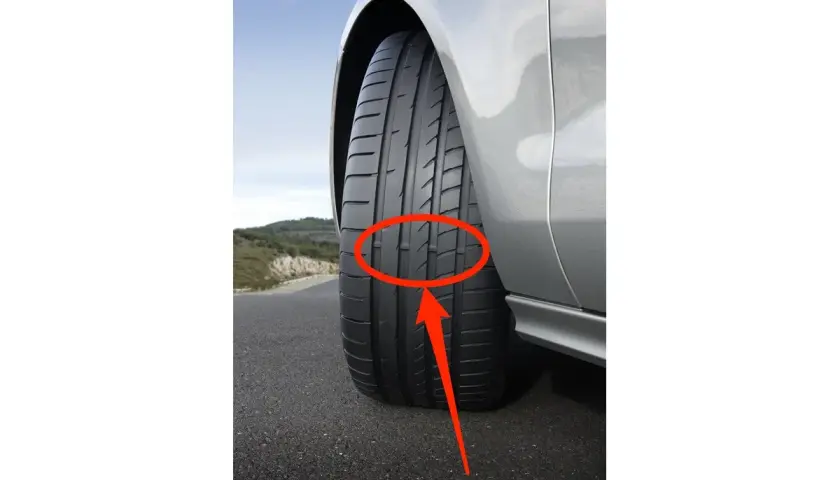Flecha roja señala los neumáticos desgastados de un coche plateado en una carretera.