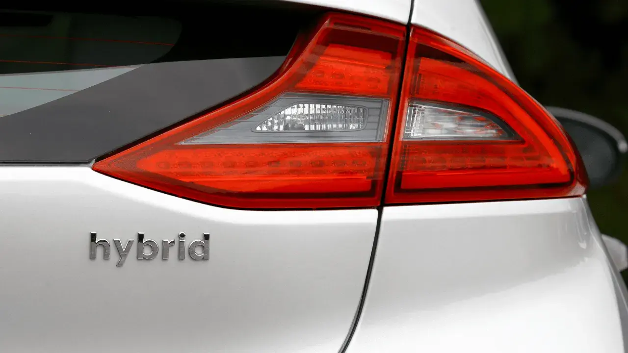 Detalle de la parte trasera de un coche blanco con la palabra "hybrid" en relieve. Las luces traseras rojas y blancas son visibles.