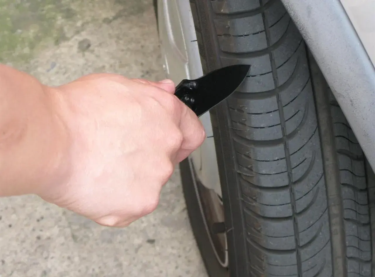 Mano con navaja revisando la banda de rodadura de un neumático, para saber si tengo una rueda pinchada.