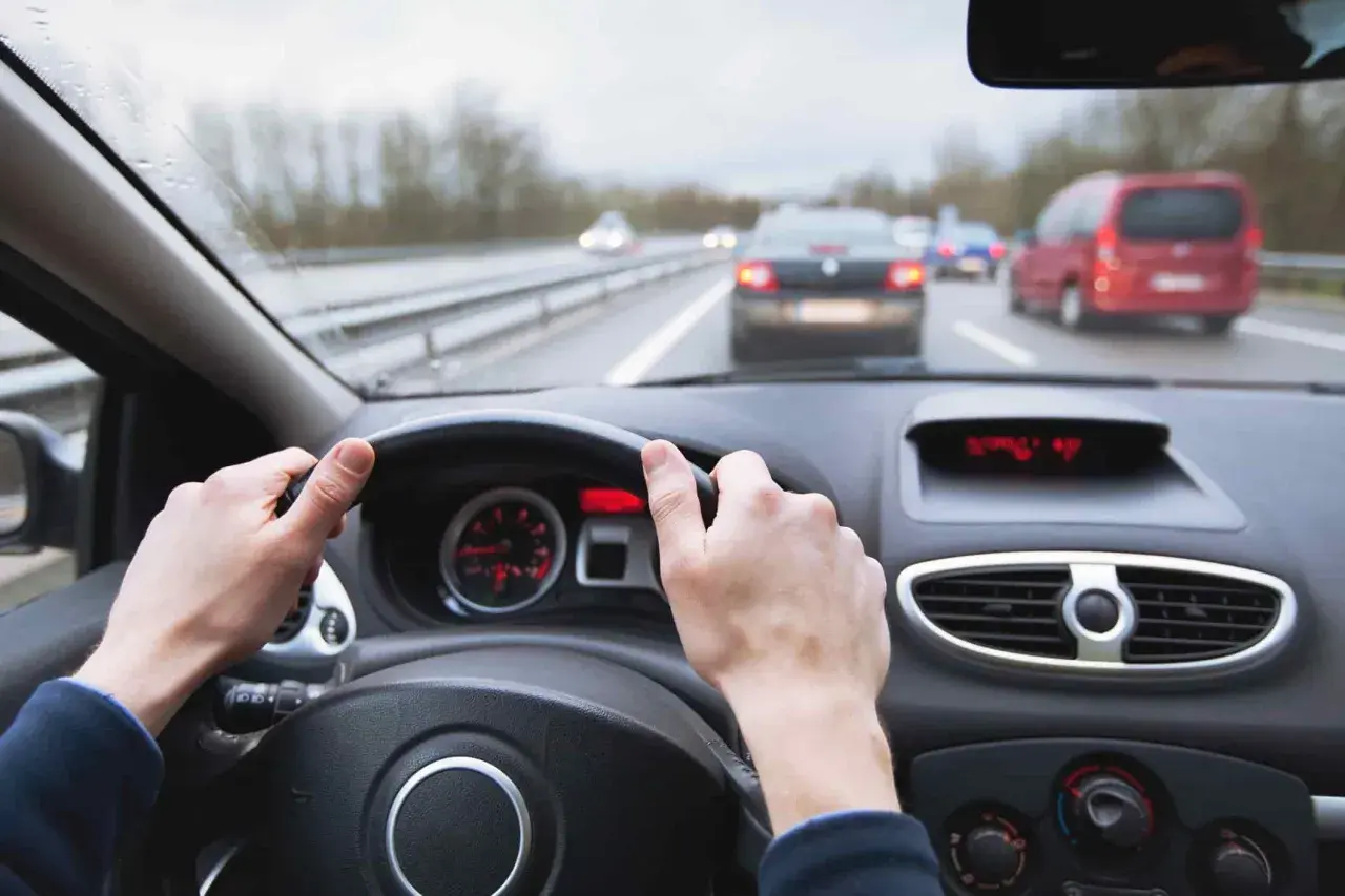 Manos al volante en carretera con tráfico. Mantener una distancia de frenado segura depende de la atención.