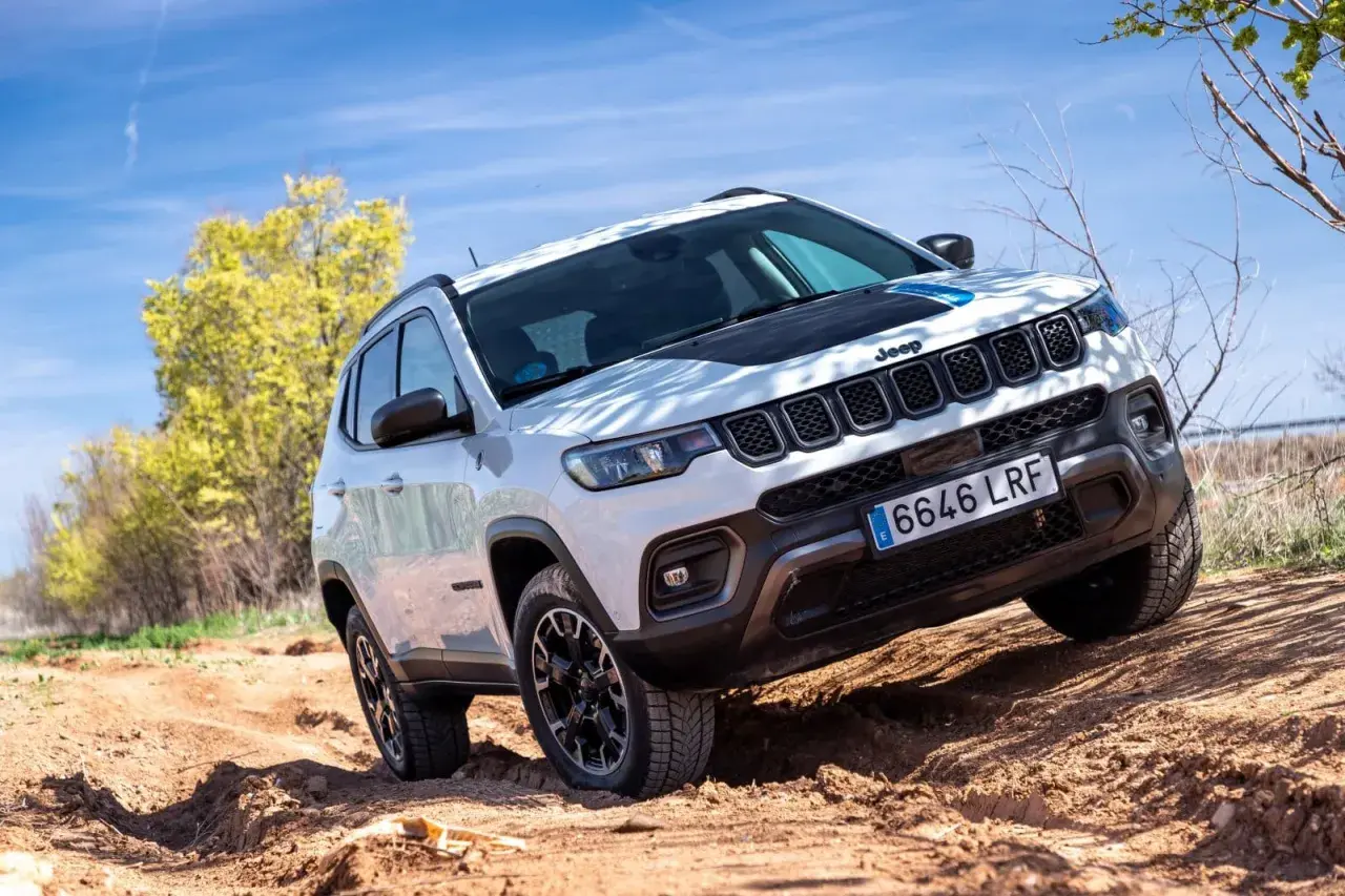 El Jeep Compass Trailhawk 4xe blanco se aventura por un camino de tierra, demostrando su capacidad todoterreno bajo un cielo azul.