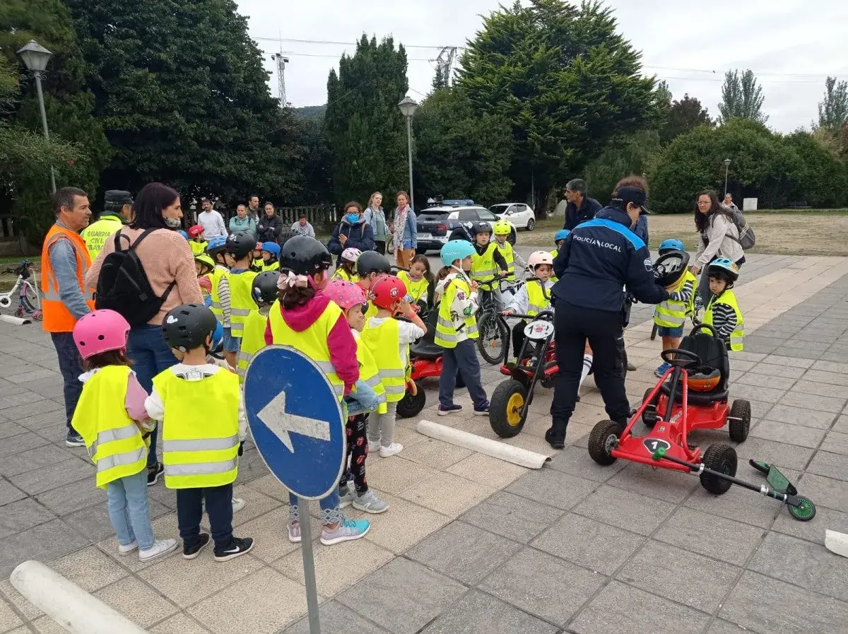 Niños con chalecos reflectantes participan en juegos de educación vial, aprendiendo normas de tráfico con bicicletas y coches de pedales.