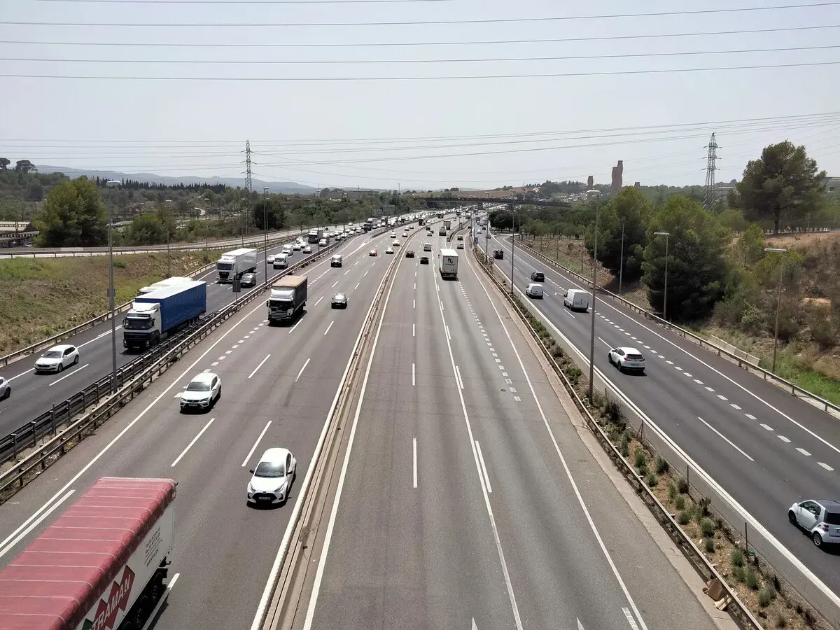 Tráfico intenso en la ap7 Girona, con camiones y coches circulando por la autopista bajo un cielo despejado.