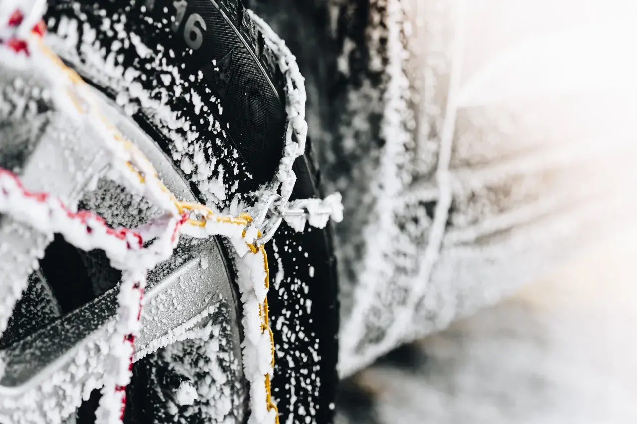 Primer plano de cadenas de nieve cubiertas de escarcha sobre un neumático de coche, mostrando cómo colocar cadenas de nieve para la seguridad invernal.