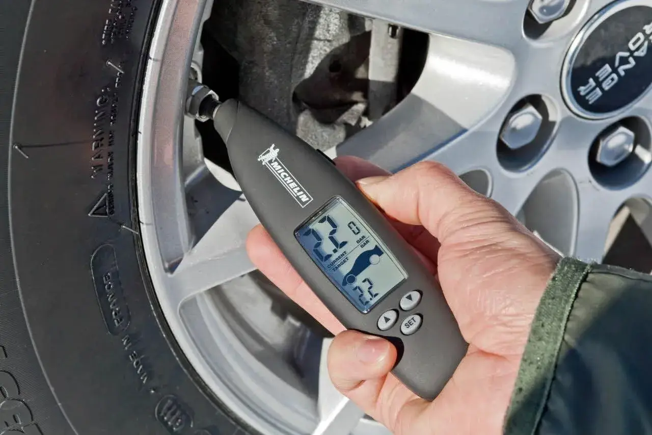 Mano revisa la presión neumaticos con un medidor digital Michelin. Muestra 2.2 bares de presión actual y objetivo.