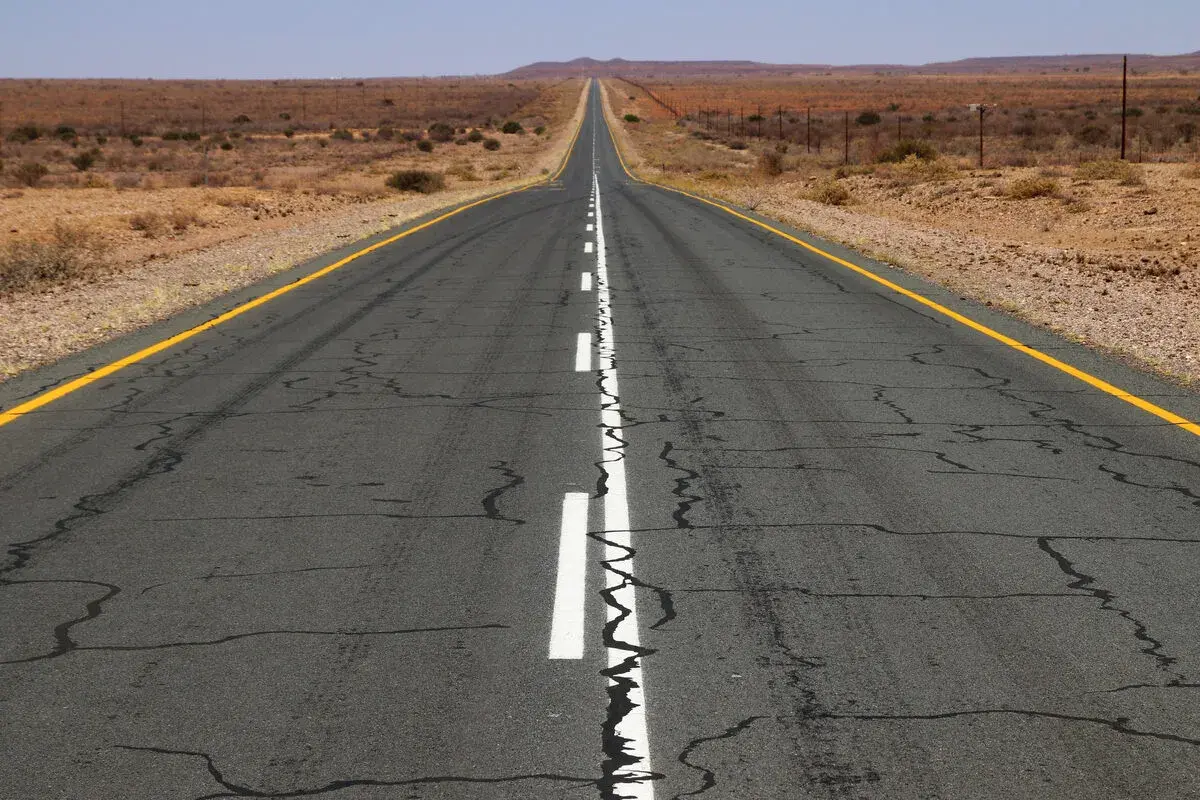 Carretera desértica con marcas longitudinales blancas y amarillas, que se pierde en el horizonte.